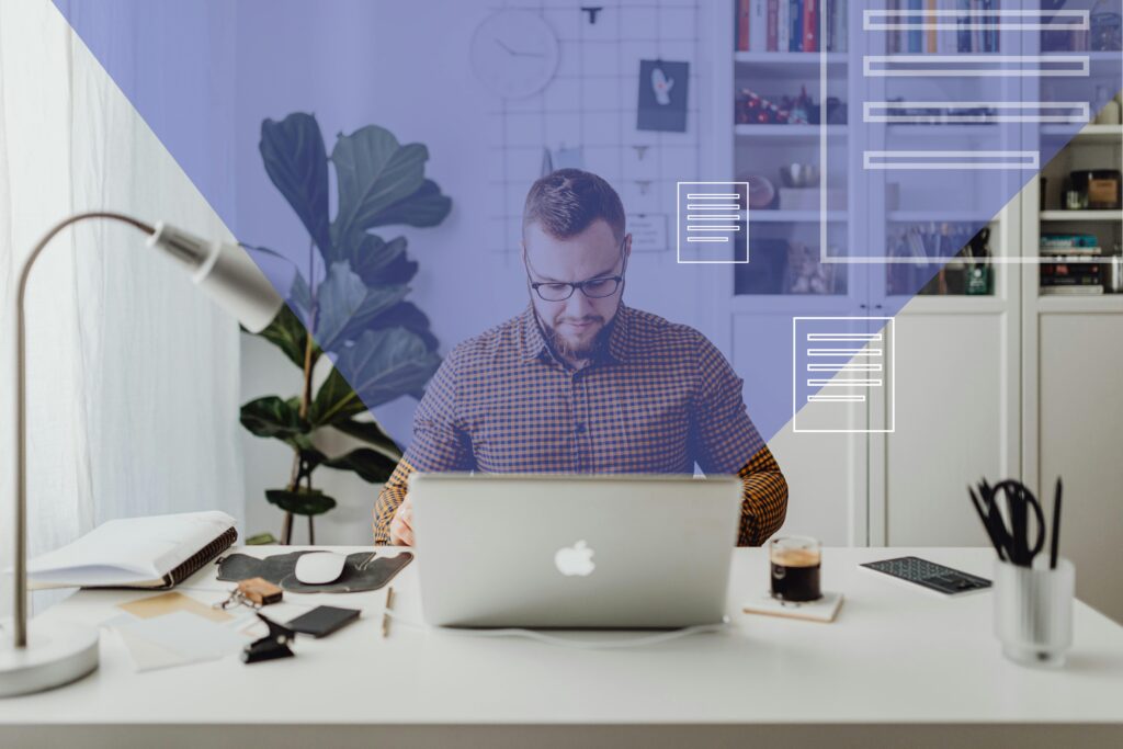 Image of a man with short hair and glasses sat at a desk. An open Mac book is in front of him with emails pinging out.
